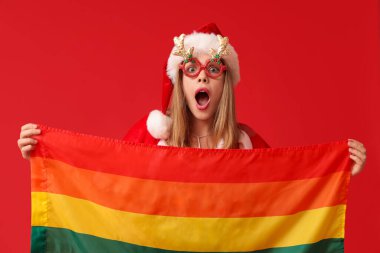 Kırmızı arka planda LGBT bayrağı olan Noel Baba kostümlü genç bir kadın şok oldu.