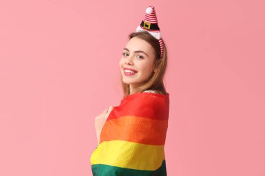 Pembe arka planda LGBT bayrağı olan Noel Baba şapkalı güzel bir kadın.