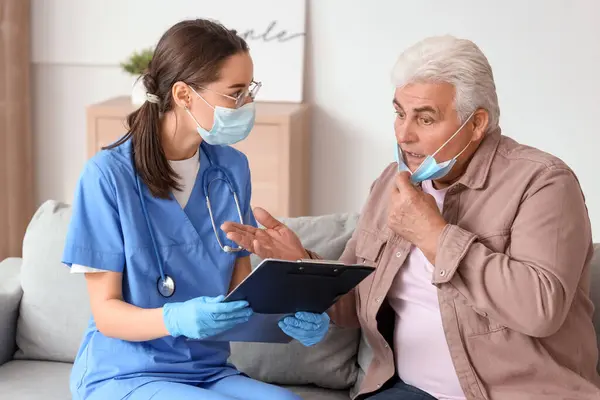 Senior man and nurse with clipboard in medical masks at home