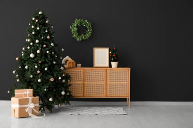Güzel bir Noel ağacı, hediyeler ve karanlık duvarın yanında ahşap bir şifonyer. Tasarım için pankart