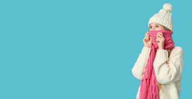 Açık mavi arka planda sıcak kış kıyafetleri içinde genç bir kız.