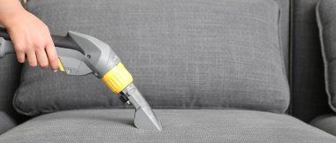 Kuru temizlemecinin çalışanı evdeki kanepedeki kiri temizliyor.