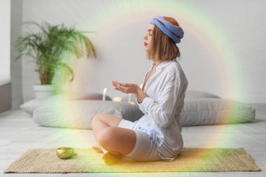 Genç kadın evde meditasyon yapıyor ve aura 'yı temizliyor.