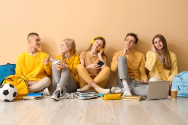 Bir grup öğrenci sarı duvarın yanında oturuyor.