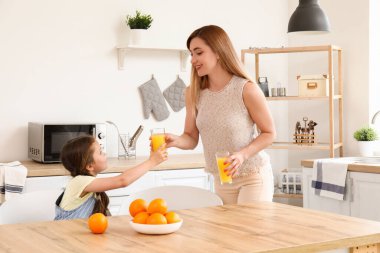Annesiyle küçük bir kız mutfakta portakal suyu içiyor.