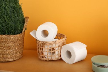 Tuvalet kağıdı ruloları ve ahşap masa üzerine saksı bitkisi olan hasır sepet. Renk duvarı yakınında, yakın plan.