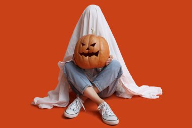 Cadılar Bayramı kostümlü kadın ve balkabağı renkli arka planda oturuyor.