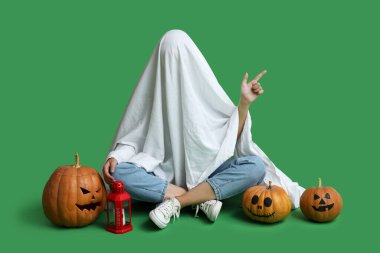 Cadılar Bayramı kostümlü, balkabaklı ve fenerli bir kadın yeşil arka plandaki bir şeyi işaret ediyor.