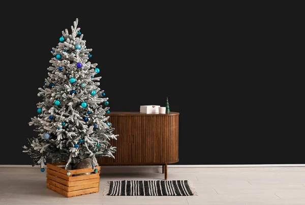 Beautiful Christmas tree with wooden dresser near dark wall. Banner for design
