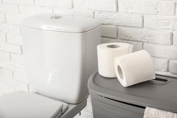 Rolls of paper rolls on toilet bowl and laundry basket near light brick wall, closeup