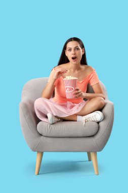 Koltuğunda patlamış mısırlı genç bir kadın mavi arka planda film izliyor.
