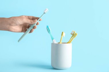 Mavi arka planda diş fırçası ve tutacağı olan kadın eli.