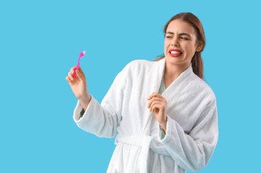 Mavi arka planda diş fırçası olan hoşnutsuz genç bir kadın.