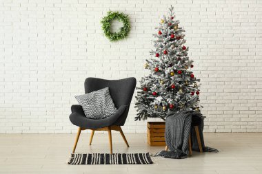 Beyaz tuğla duvarın yanında koltukları olan güzel Noel ağacı