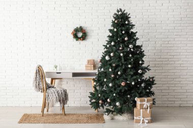 Masası ve beyaz tuğla duvarın yanında hediye kutuları olan güzel Noel ağacı.