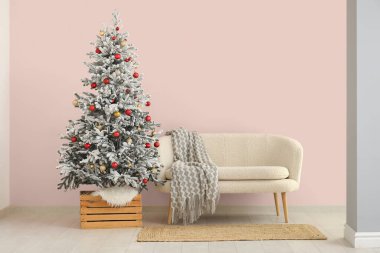 Pembe duvarın yanında kanepesi olan güzel bir Noel ağacı