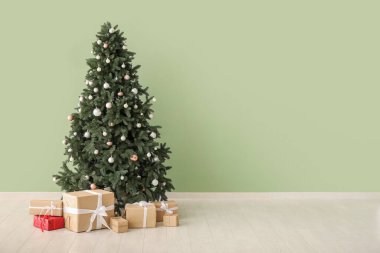 Yeşil duvarın yanında hediye kutuları olan güzel Noel ağacı