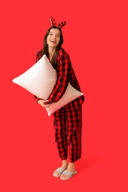 Kareli pijamalı ve kırmızı arka planda yumuşak yastıklı ren geyiği boynuzlu güzel bir kadın.