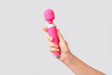 Gri arka planda pembe vibratörlü kadın eli, yakın plan.
