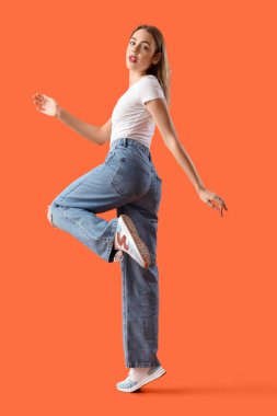 Turuncu arka planda modaya uygun kot giyen genç bir kadın.