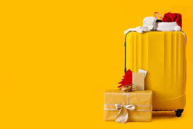 İçinde Noel hediyesi ve sarı arka planda seyahat aksesuarları olan bavul.