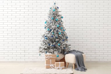Güzel Noel ağacı, hediye kutuları ve yumuşak tuğla duvarın yanında puf.