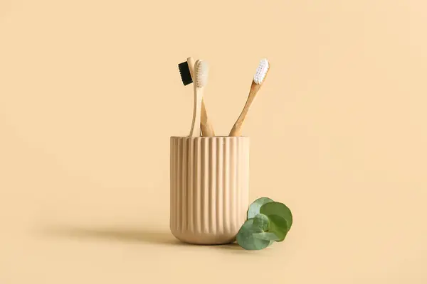 Wooden toothbrushes in holder with eucalyptus branch on beige background.