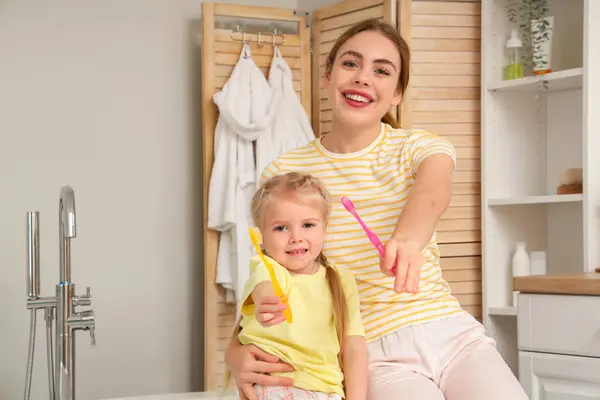若い母親と彼女の小さな娘は バスルームに歯ブラシを持っています — ストック写真