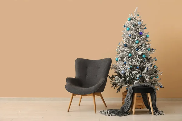 Beautiful Christmas tree with armchairs near beige wall