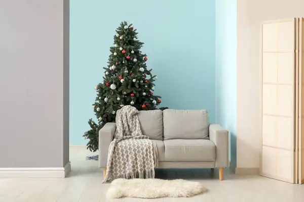 Beautiful Christmas tree with sofa near blue wall