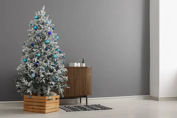Beautiful Christmas tree with dresser near grey wall