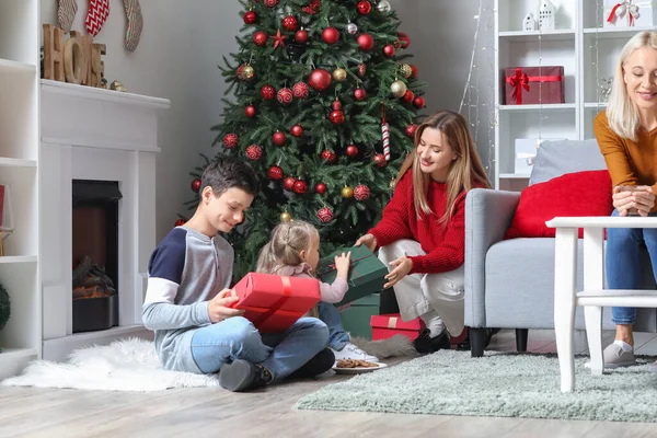 Happy mother giving Christmas presents to her little children at home
