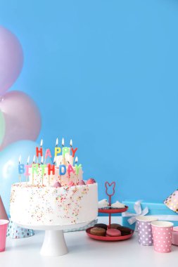 Mavi duvarın yanındaki masada farklı tatlılar olan doğum günü pastası.