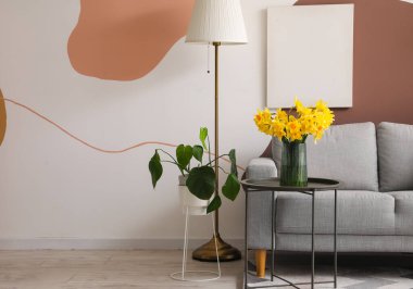 Şık oturma odasının içinde rahat gri kanepe ve kahve masasında çiçek açan narsisli çiçekler.