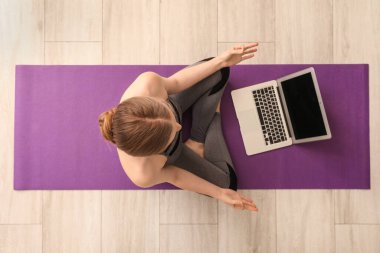 Dizüstü bilgisayarlı genç bir kadın spor salonunda yoga yapıyor.