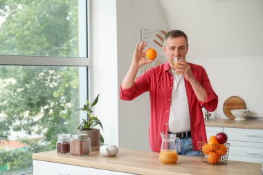 Mutfakta portakal suyu içen olgun bir adam.