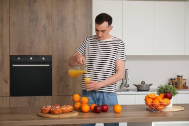 Genç adam mutfakta portakal suyunu bardağa dolduruyor.