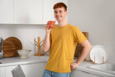 Genç kızıl saçlı adam mutfakta meyve suyu içiyor.