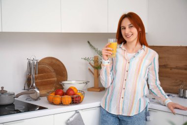 Mutfakta bir bardak meyve suyu olan genç kızıl saçlı kadın.