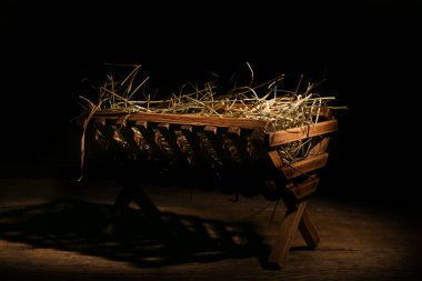 Manger with hay on wooden table against dark background clipart