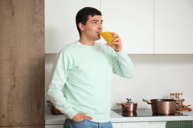 Genç adam mutfakta portakal suyu içiyor.
