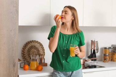 Mutfakta bir bardak meyve suyu ve portakal suyu olan genç bir kadın.