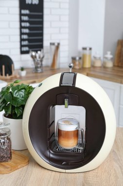 Modern coffee machine with glass cup of hot latte on table in kitchen