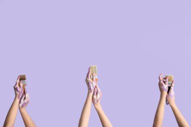 Leylak arka planında boya fırçası olan kadın eller.