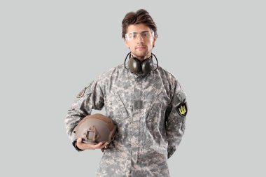 Gri arka planda kaskı olan genç bir erkek asker.