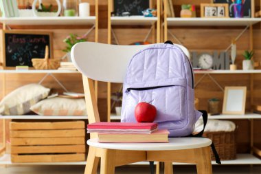 Okul çantası, kitaplar ve sandalyede elma.