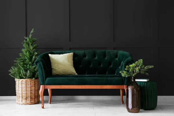 Stylish green sofa with Christmas tree near dark wall in room