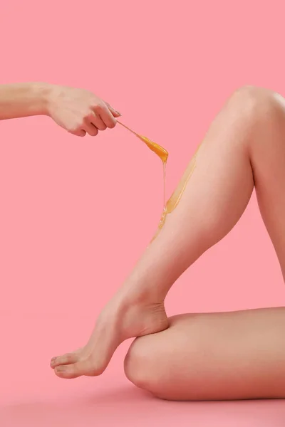 Hand applying sugaring paste onto young woman\'s legs against pink background