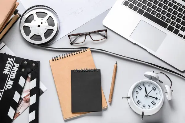 Notebooks with film reel, movie clapper, alarm clock and laptop on grey background