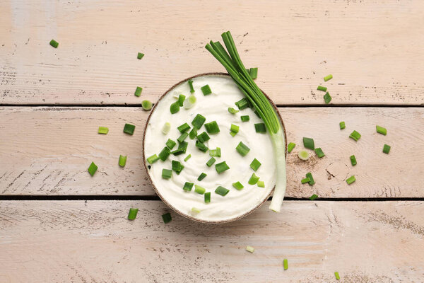 Чаша вкусной сметаны с зеленым луком на светлом деревянном фоне